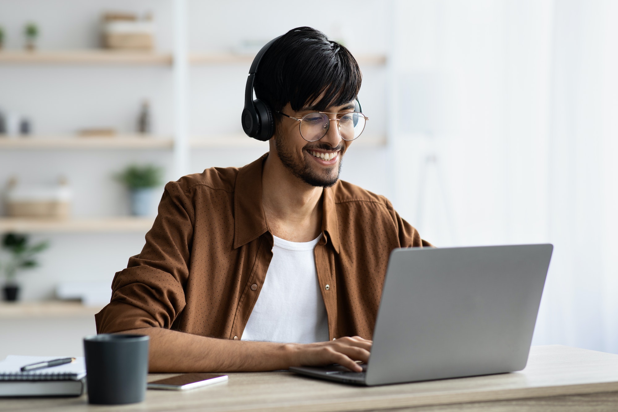 Smiling indian guy attending webinar, typing on laptop keyboard